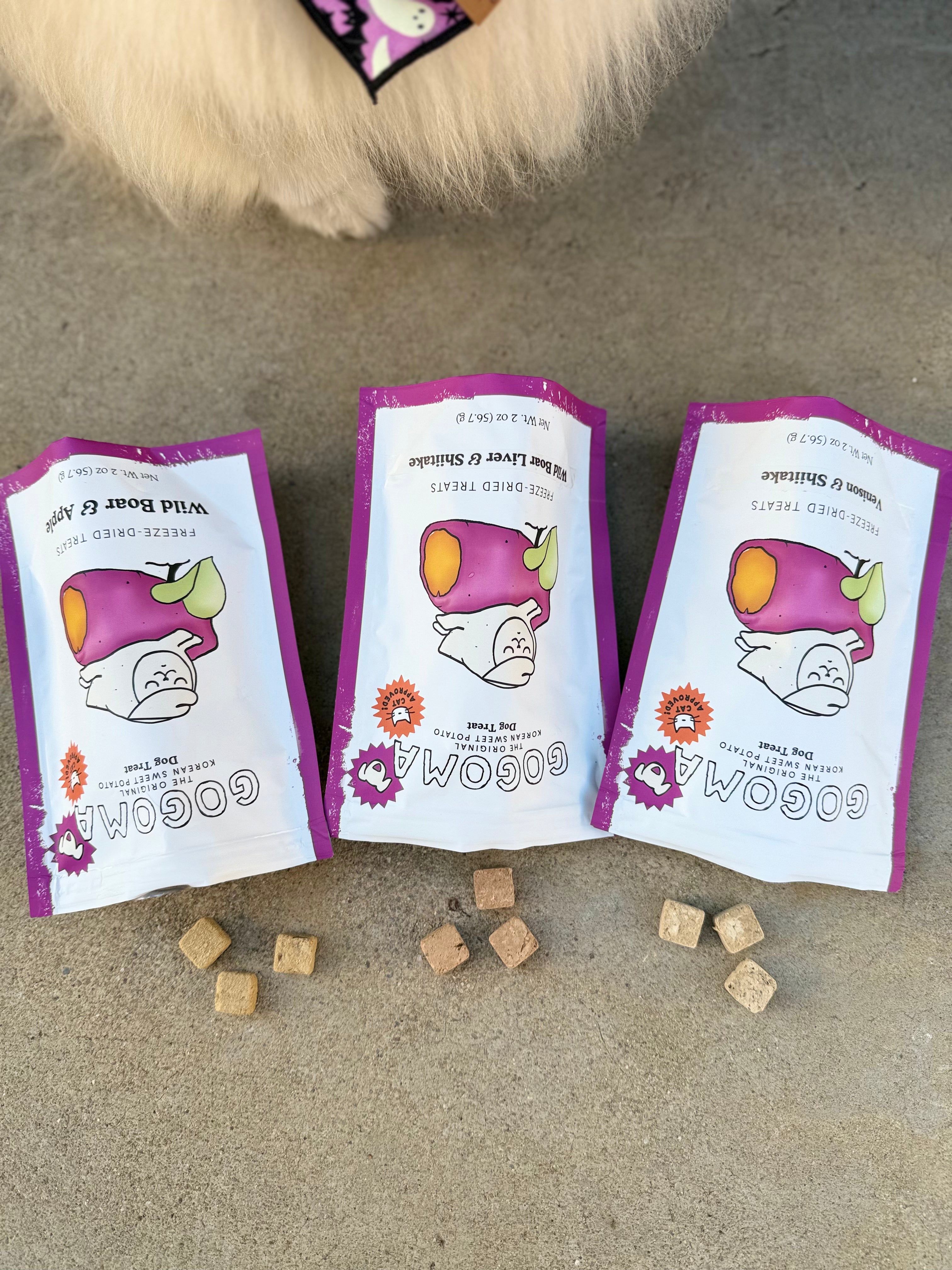 Three Gogoma freeze-dried treats pouches on a concrete surface with a dog's paw in the background.