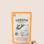 A stand-up pouch of Gogoma freeze-dried pet treats on a warm beige background, with several small bite-sized treats placed in front of the package. The package is white with orange border and printed black and orange text and illustrations of an elk and sweet potato.