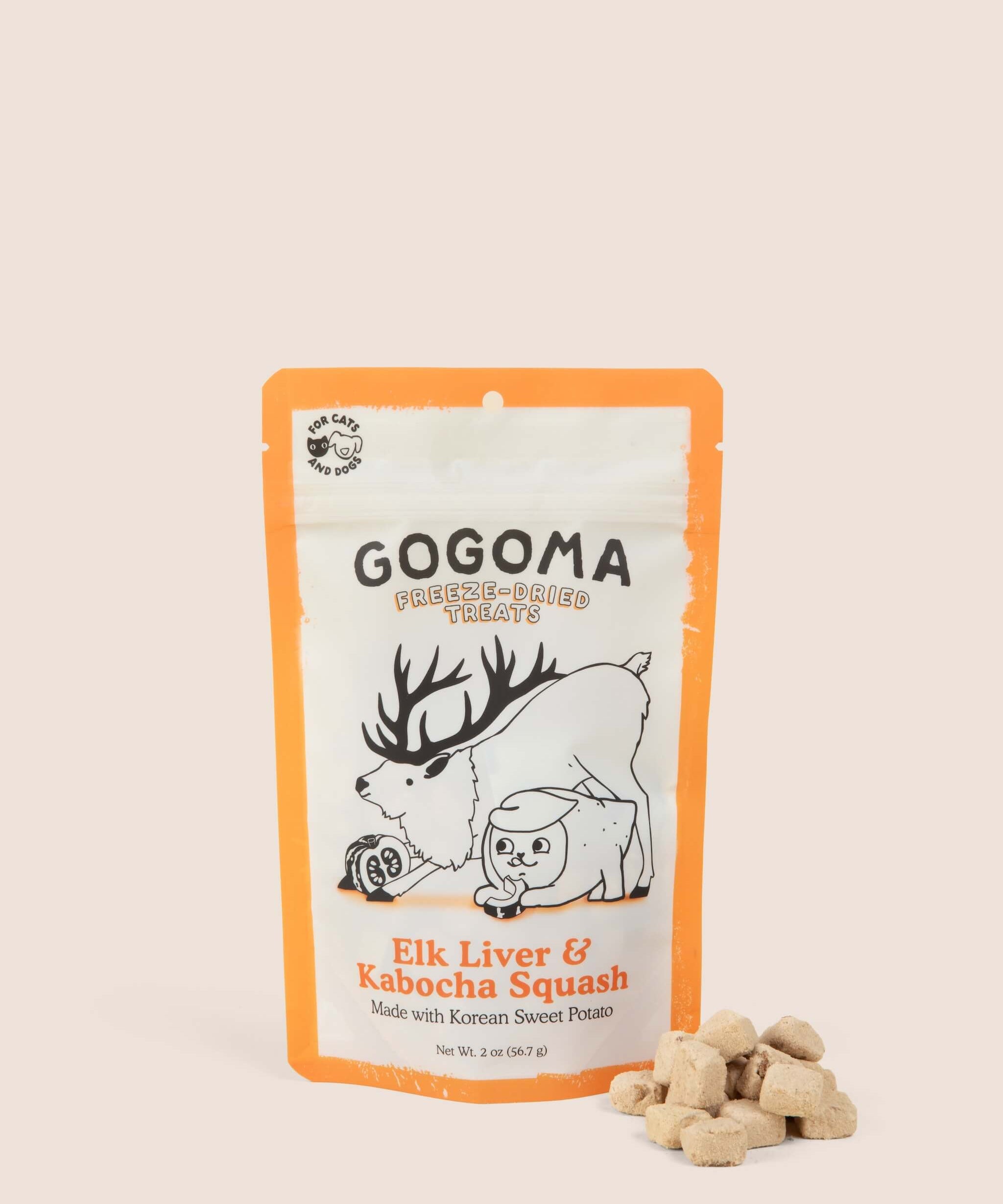 A stand-up pouch of Gogoma freeze-dried pet treats on a warm beige background, with several small bite-sized treats placed in front of the package. The package is white with orange border and printed black and orange text and illustrations of an elk and sweet potato.