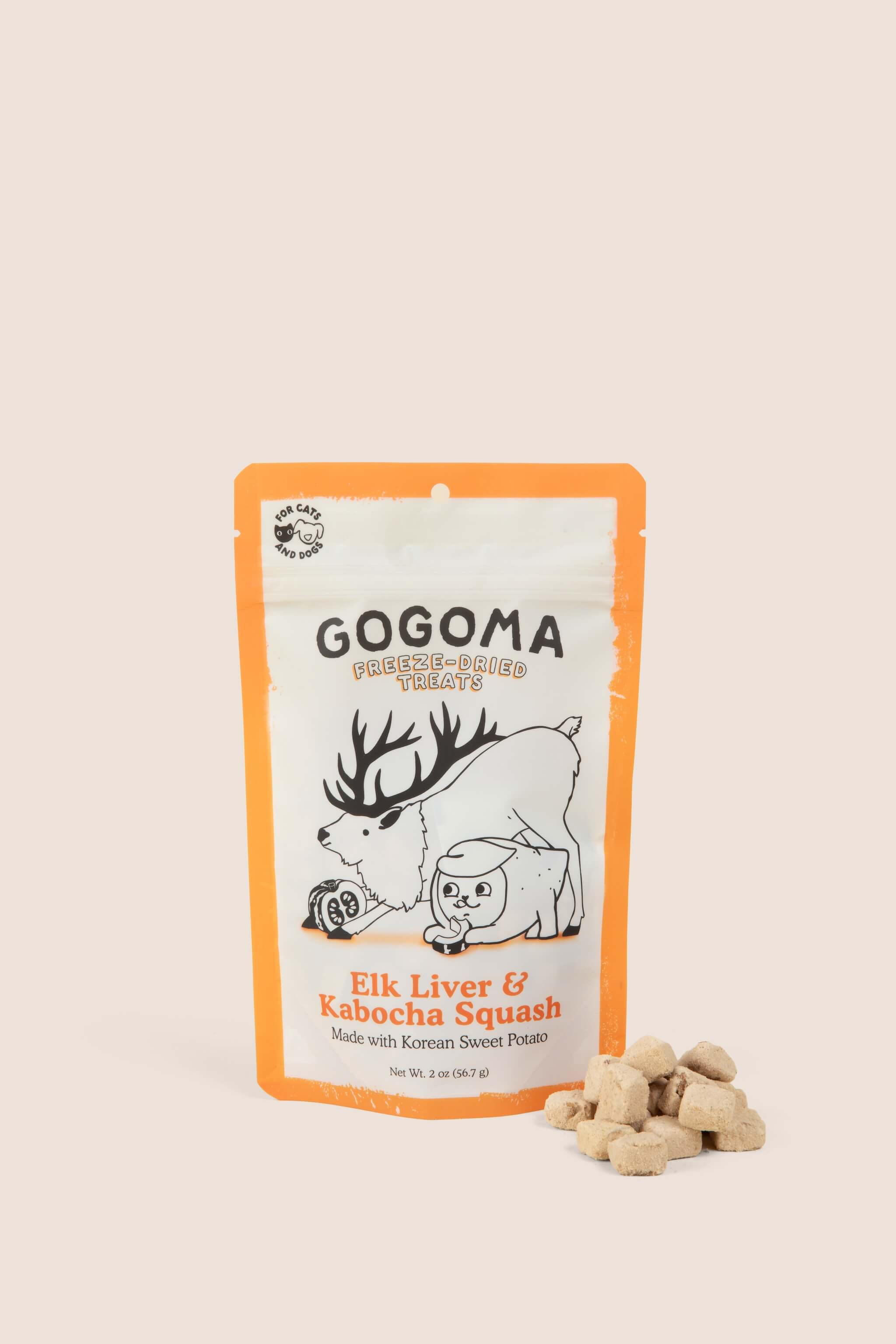 A stand-up pouch of Gogoma freeze-dried pet treats on a warm beige background, with several small bite-sized treats placed in front of the package. The package is white with orange border and printed black and orange text and illustrations of an elk and sweet potato.