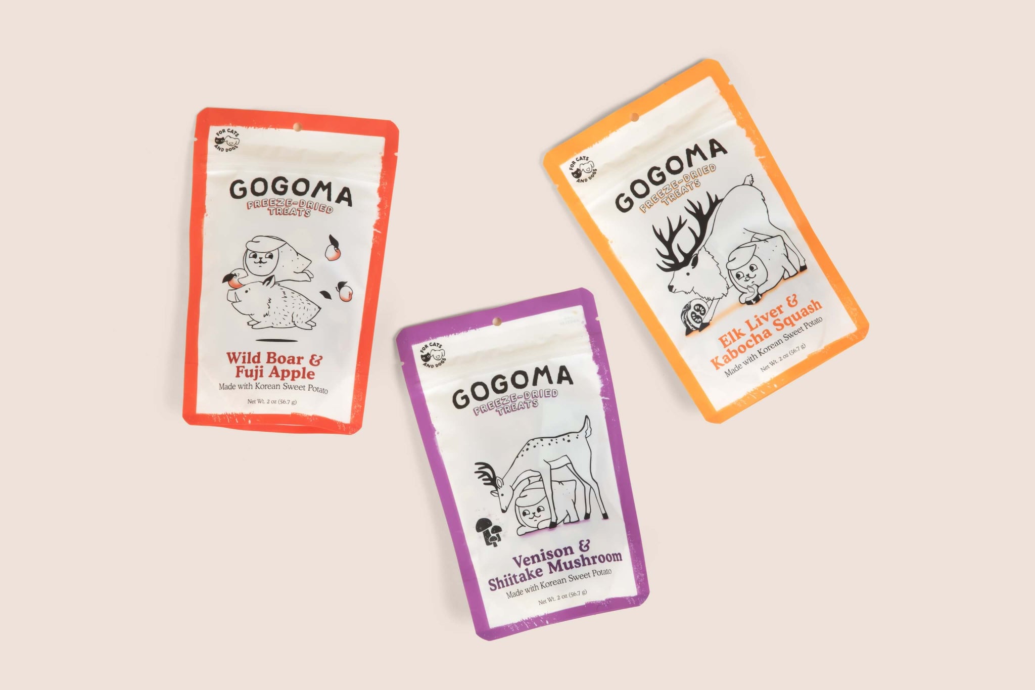 Three GOGOMA freeze-dried pet treat pouches arranged on a light beige background: a red-bordered Wild Boar & Fuji Apple pouch, an orange-bordered Elk Liver & Kabocha Squash pouch, and a purple-bordered Venison & Shiitake Mushroom pouch.