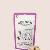 A stand-up pouch of GOGOMA freeze-dried pet treats on a light beige background, with several bite-sized, cube-shaped treats placed in front of the package. The package is white with a purple border. black text, and  illustration of a deer and sweet potato.