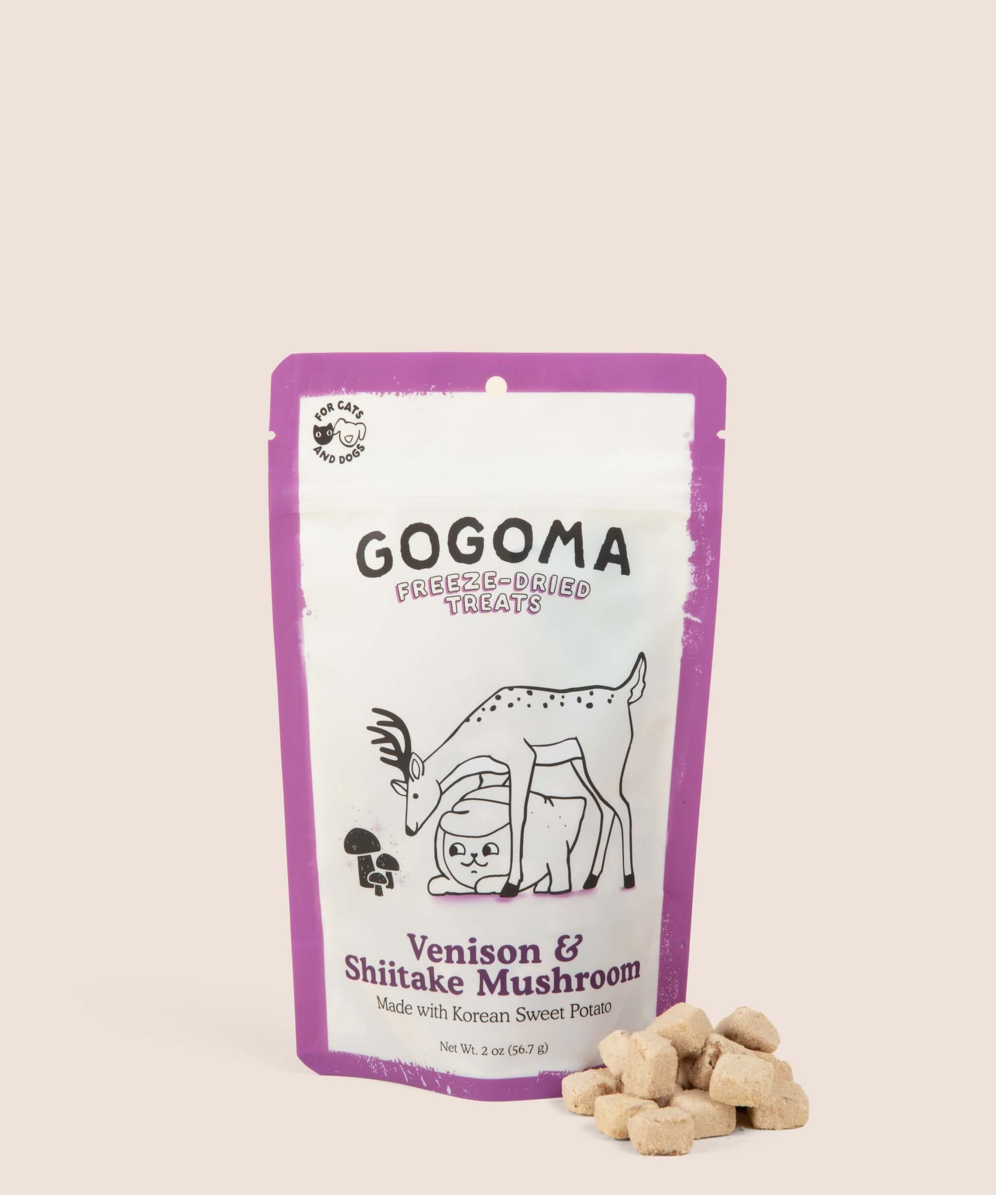 A stand-up pouch of GOGOMA freeze-dried pet treats on a light beige background, with several bite-sized, cube-shaped treats placed in front of the package. The package is white with a purple border. black text, and  illustration of a deer and sweet potato.
