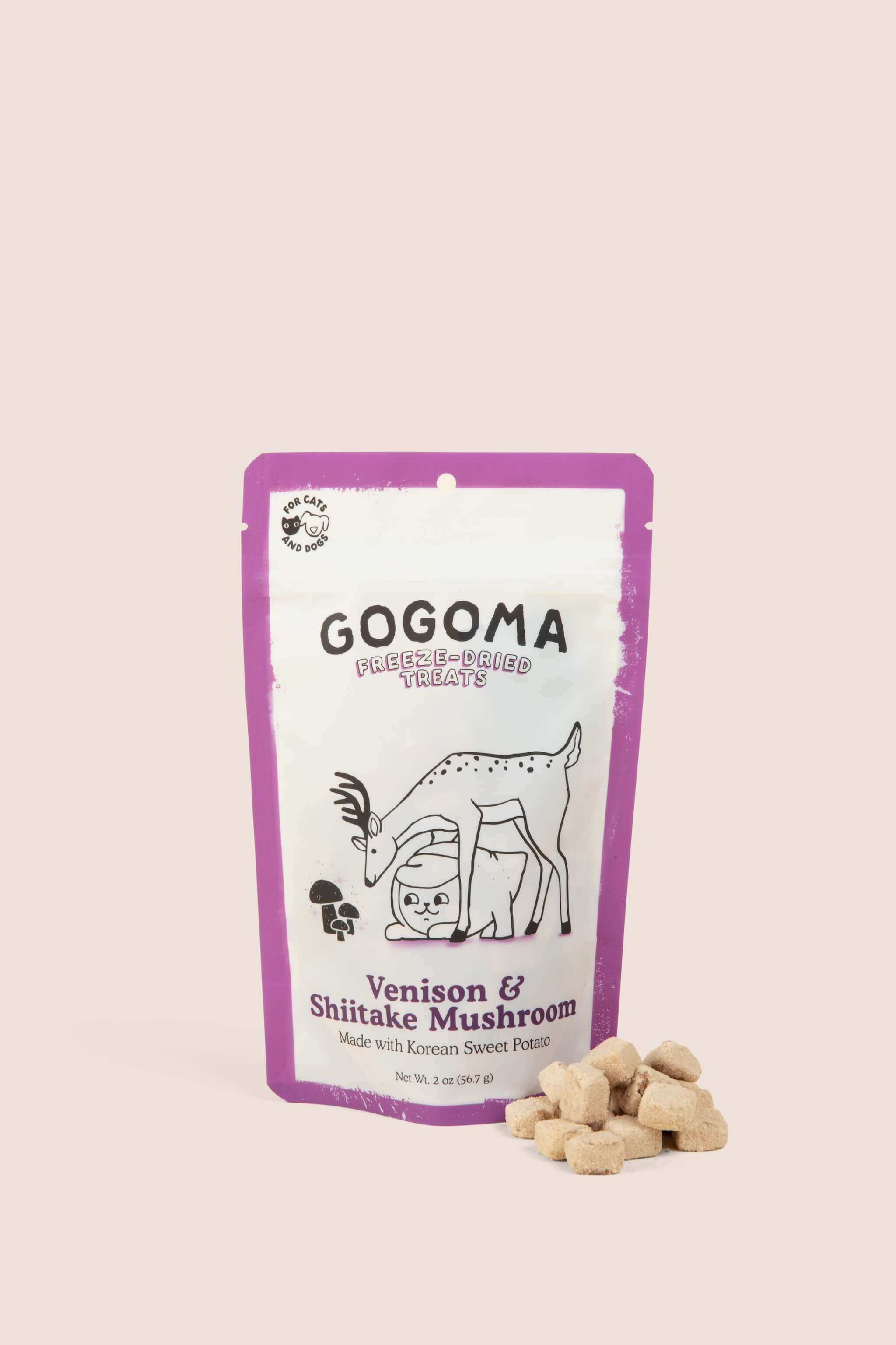 A stand-up pouch of GOGOMA freeze-dried pet treats on a light beige background, with several bite-sized, cube-shaped treats placed in front of the package. The package is white with a purple border. black text, and  illustration of a deer and sweet potato.