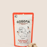 A stand-up pouch of GOGOMA freeze-dried pet treats on a warm beige background, with several small cube-shaped treat bites placed in front of the package. The package has a red border and a white center with black text reading GOGOMA at top of pouch and red text reading Wild Boar & Fuji Apple on bottom of pouch and an illustration of a boar and sweet potato.